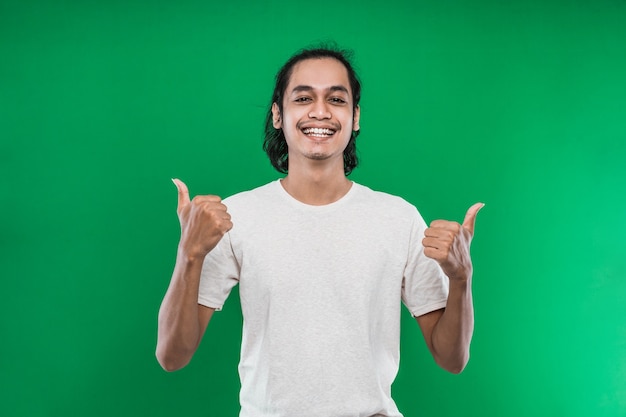 Homem bonito, levantando as duas mãos enquanto mostra os polegares para a câmera sorrindo, isolado em um fundo verde