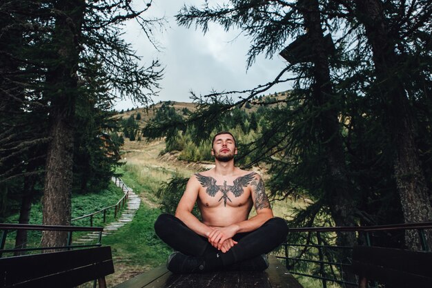 Homem bonito, meditando na mesa na floresta