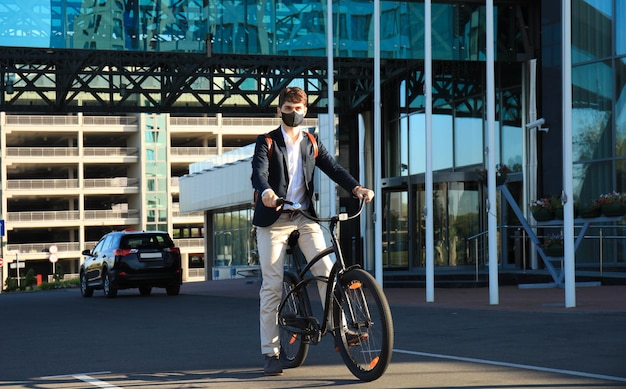 Homem bonito na máscara protetora, andando de bicicleta para encontrar emprego.