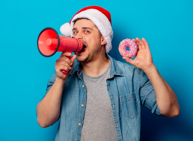 Homem bonito no chapéu de Natal com donut e alto-granizo