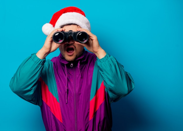 Homem bonito no chapéu de Natal e jaqueta dos anos 90 com binóculos