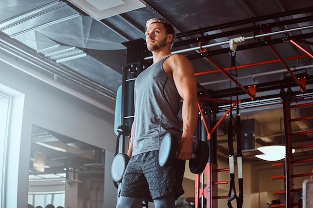 Foto homem bonito no sportswear detém halteres no clube de fitness ou ginásio.