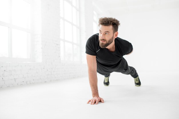 Homem bonito no sportswear preto segurando uma prancha no interior branco do ginásio