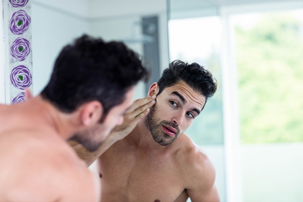 Homem bonito olhando para o cabelo no banheiro