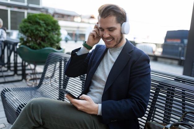 Homem bonito ouvindo música em fones de ouvido de um celular com um sorriso no rosto enquanto