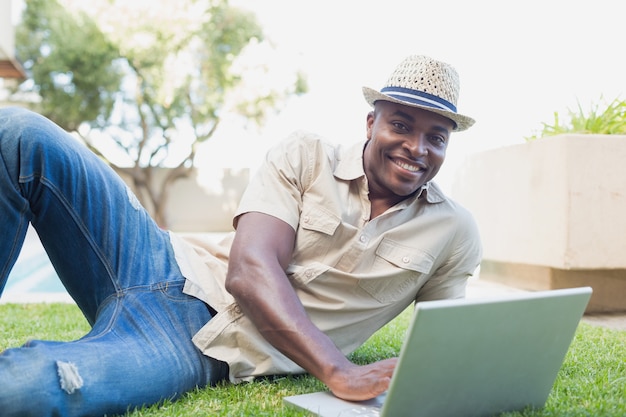 Homem bonito que relaxa em seu jardim usando laptop