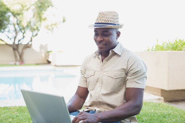 Homem bonito que relaxa em seu jardim usando laptop