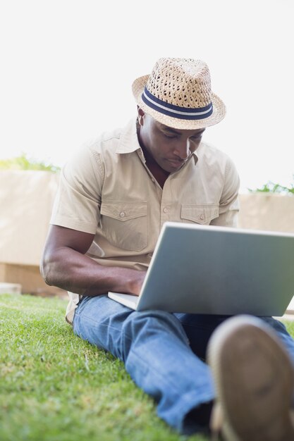 Homem bonito que relaxa em seu jardim usando laptop