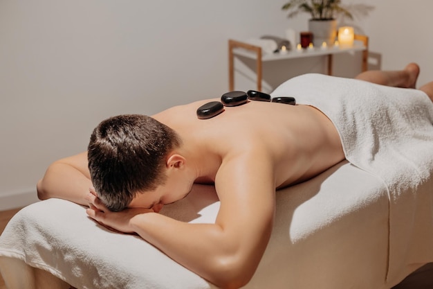 Homem bonito relaxante durante a massagem nas costas com pedras quentes. cuidados com o corpo e spa no resort