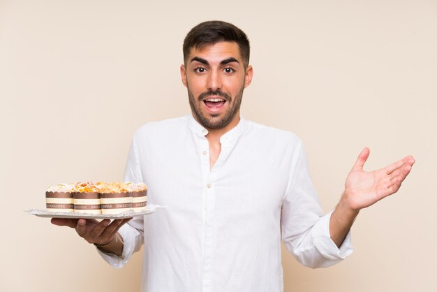 Homem bonito, segurando o bolo queque sobre parede isolada com expressão facial chocado