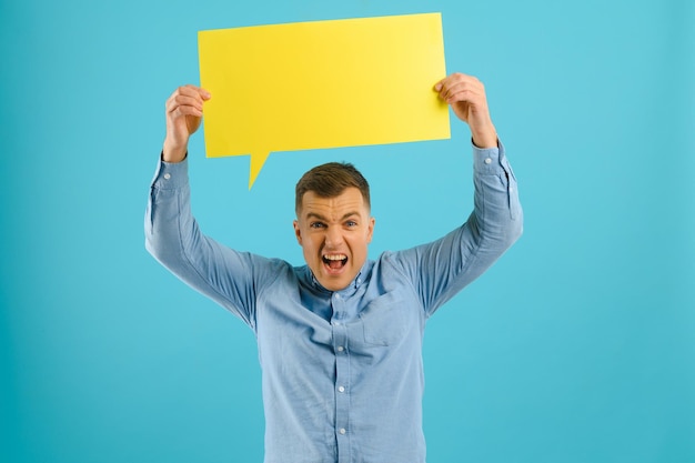 Homem bonito segurando um cartaz de balão de fala em branco, isolado no fundo amarelo do estúdio