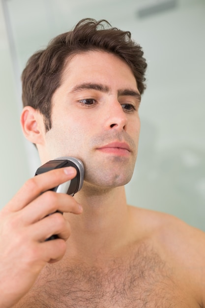 Homem bonito sem camisa, fazer a barba com barbeador elétrico