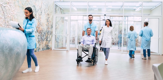 Foto homem bonito sênior em uma cadeira de rodas está se mudando para o hospital com a ajuda de uma equipe médica especial