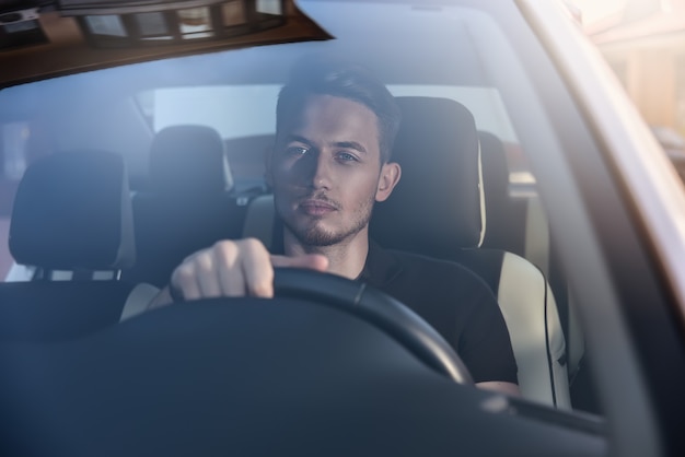 Homem bonito sentado em um carro e segurando o volante.