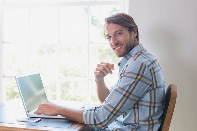 Homem bonito sentado na mesa usando laptop