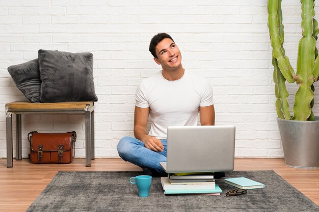 Homem bonito sentado no chão com seu laptop rindo e olhando para cima