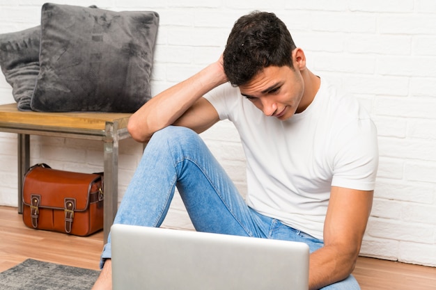 Homem bonito, sentado no chão com seu laptop