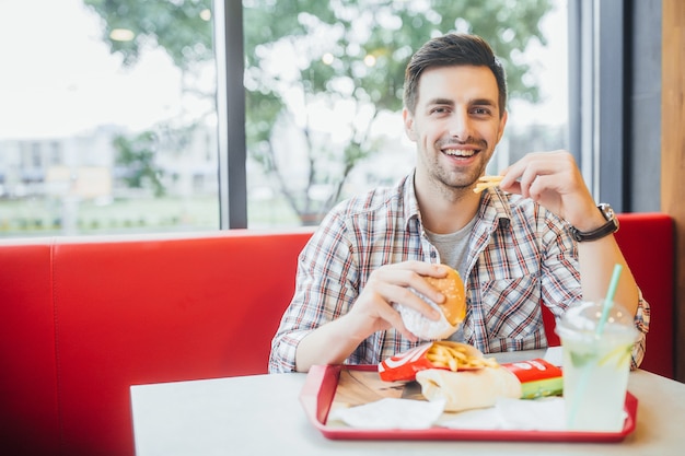 Homem bonito sentado no restaurante moderno fast-food e jantar