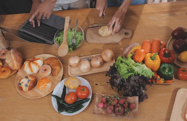 Homem bonito sentado perto de sua esposa na cozinha Casal da família vê mídia social navegar na web enquanto está sentado na mesa da cozinha com laptop genérico Casal trabalhando com laptop em casa