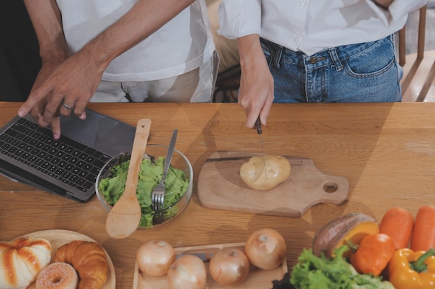 Homem bonito sentado perto de sua esposa na cozinha Casal de família vê mídias sociais navegando na web enquanto está sentado na mesa da cozinha com um laptop genérico Casal trabalhando com laptop em casa