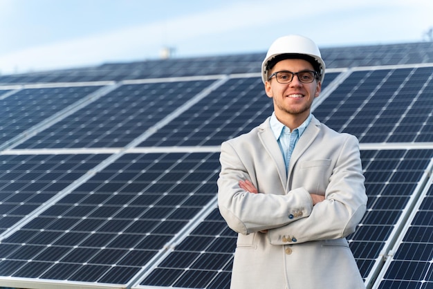 Homem bonito sorridente no capacete posando para a câmera fotográfica perto das baterias de energia solar ao ar livre