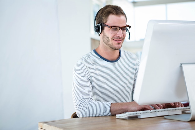 Homem bonito, trabalhando no computador com fone de ouvido em um escritório brilhante