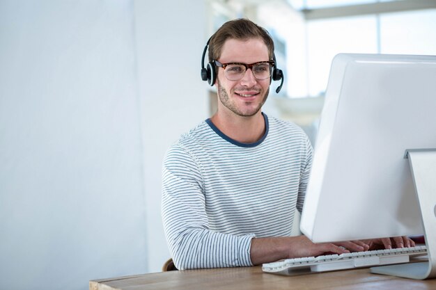 Homem bonito, trabalhando no computador com fone de ouvido em um escritório brilhante