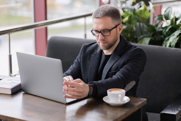 Homem bonito, trabalhando no laptop para uma xícara de café em um restaurante