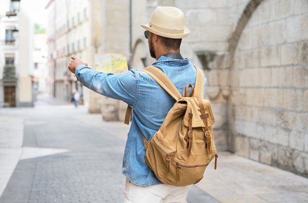 Homem bonito turista olhar para o mapa enquanto aponta o dedo na direção do conceito de viagem de destino ...