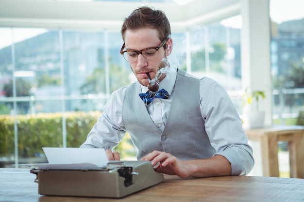 Homem bonito, usando a máquina de escrever à moda antiga no escritório brilhante