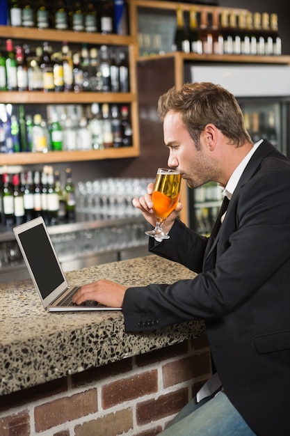 Homem bonito usando computador portátil e bebendo uma cerveja