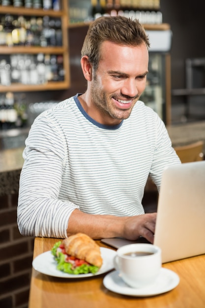 Homem bonito usando laptop e tendo um croissant