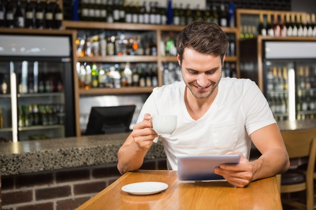 Homem bonito usando tablet e tomando café