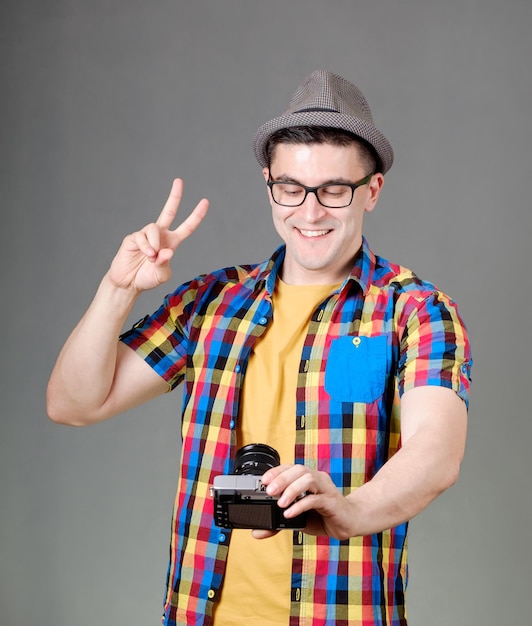 Homem bonito, vestido com uma camisa multicolorida, tirando selfie com câmera fotográfica isolada em fundo cinza