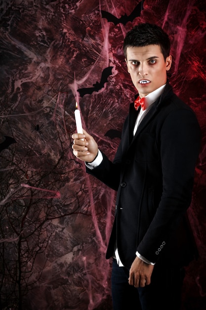 Foto homem bonito vestido com uma fantasia de drácula para o halloween. vampiro atraente com velas