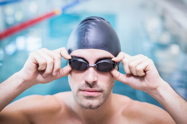 Homem bonito vestindo boné de natação e óculos de proteção na piscina