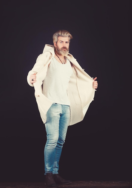 Homem bonito vestindo calças jeans e um casaco posando no estúdio Moda sazonal de beleza masculina