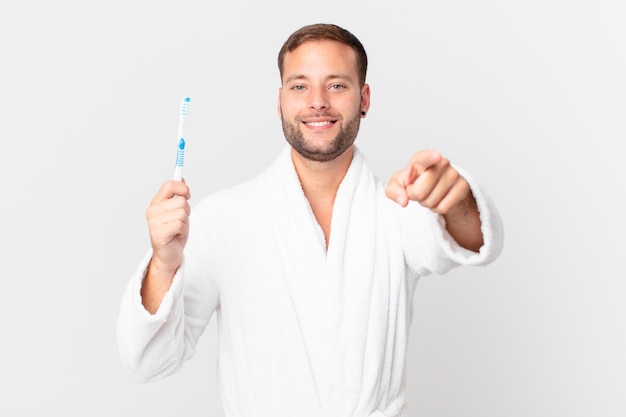 Homem bonito vestindo roupão de banho e segurando uma escova de dentes