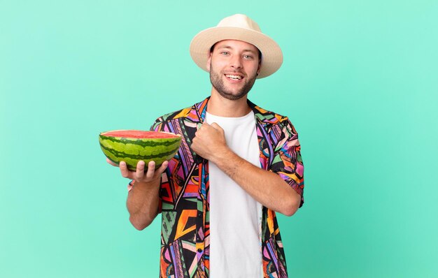 Homem bonito viajante se sentindo feliz e enfrentando um desafio ou comemorando e segurando um conceito de férias de melancia