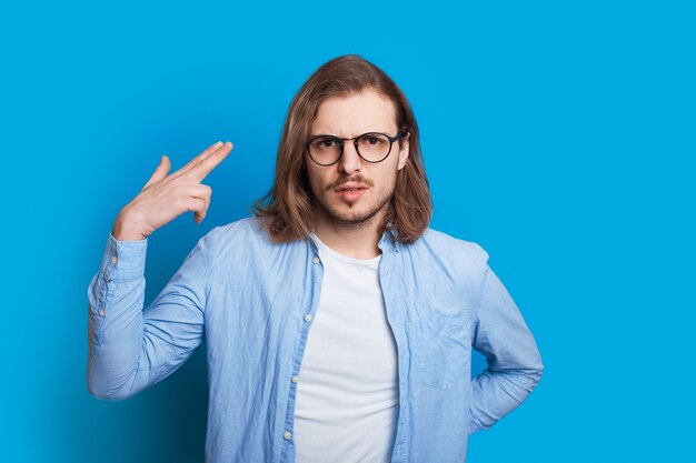 Homem branco com cabelo comprido e óculos gesticulando com a mão como se estivesse atirando