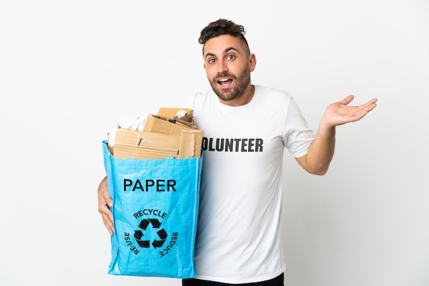 Homem branco segurando uma sacola cheia de papel para reciclar isolado no fundo branco com expressão facial chocada