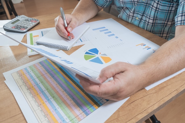 Homem branco sentado fazendo contas com uma calculadora e revisando fluxos de caixa e de dinheiro, projeções e faturas. Trabalho de conceito em casa, contas correntes, economia doméstica.