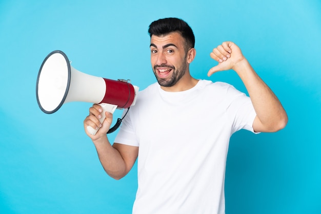 Homem branco sobre fundo azul isolado segurando um megafone e orgulhoso e satisfeito consigo mesmo