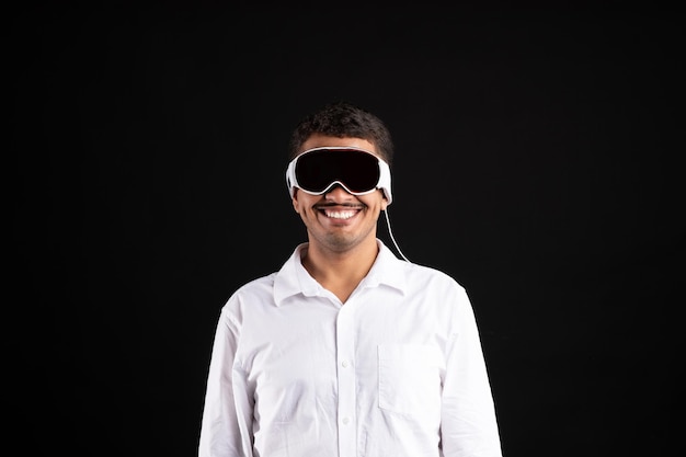 Homem brasileiro alegre em camisa usando óculos vision pro vr usando gadget moderno no estúdio preto