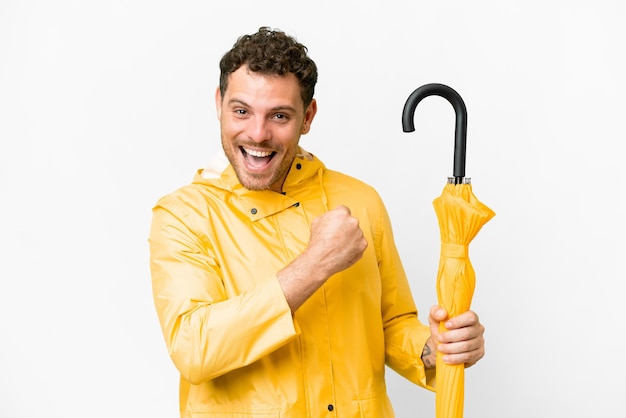 Homem brasileiro com casaco à prova de chuva e guarda-chuva sobre fundo branco isolado comemorando uma vitória