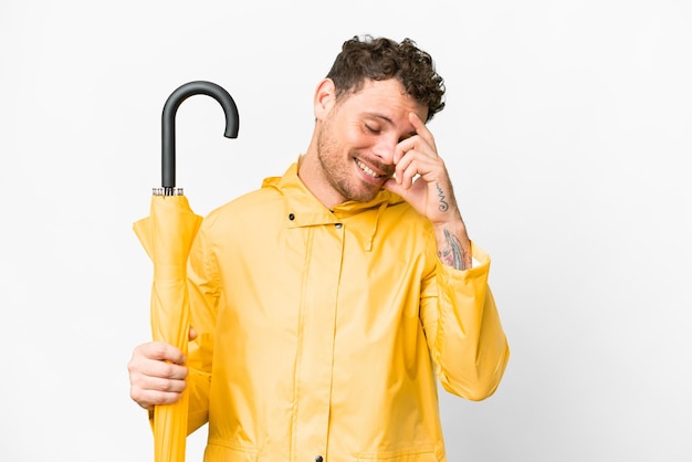 Homem brasileiro com casaco à prova de chuva e guarda-chuva sobre fundo branco isolado rindo