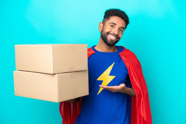 Homem brasileiro de entrega de super-herói isolado em fundo azul, estendendo as mãos para o lado para convidar para vir