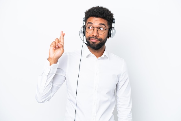 Homem brasileiro de telemarketing trabalhando com um fone de ouvido isolado em fundo branco com dedos cruzando e desejando o melhor