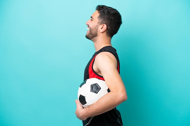 Homem brasileiro do jovem jogador de futebol isolado no fundo azul rindo na posição lateral