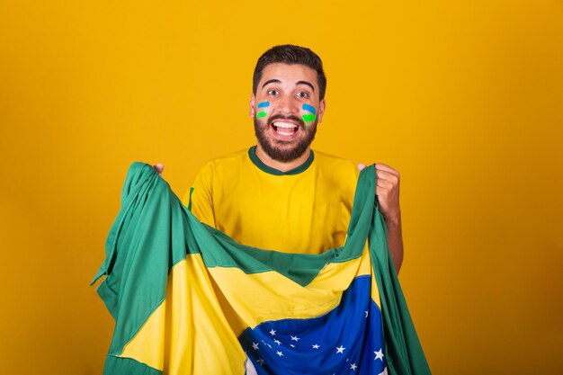 Foto homem brasileiro latino-americano torcendo pelo brasil na copa do mundo 2022 patriota nacionalista vibrando a bandeira do brasil torcendo e pulando símbolo de felicidade alegria e celebração com a bandeira do brasil